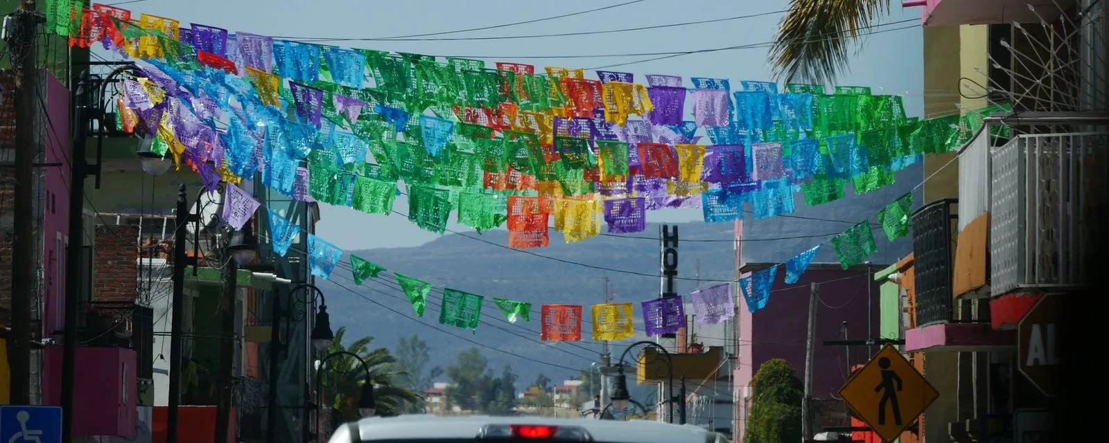 Una calle de Calvillo cruzada por hileras de papel picado de colores, con las casas del pueblo a los lados y los cerros al fondo