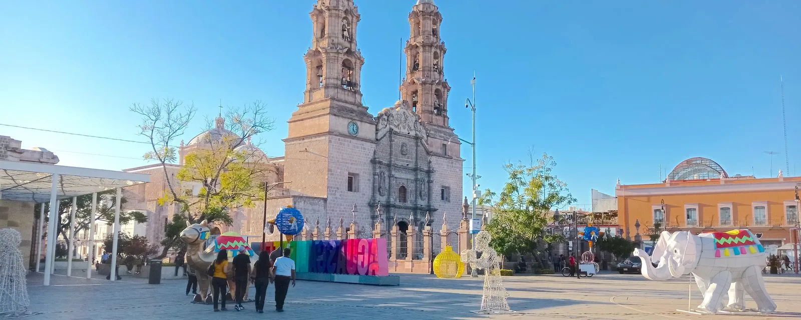 La Catedral Basílica de Aguascalientes con sus dos torres de cantera al fondo de la Plaza de la Patria, con gente cruzando la explanada
