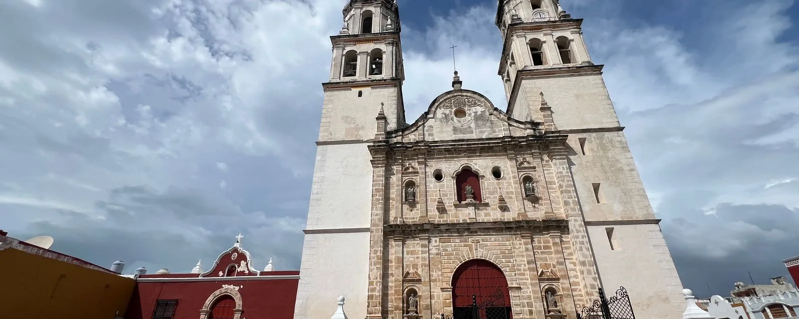 La catedral de San Francisco de Campeche vista desde la plaza: sus dos torres blancas y la portada de cantera contra un cielo cargado de nubes