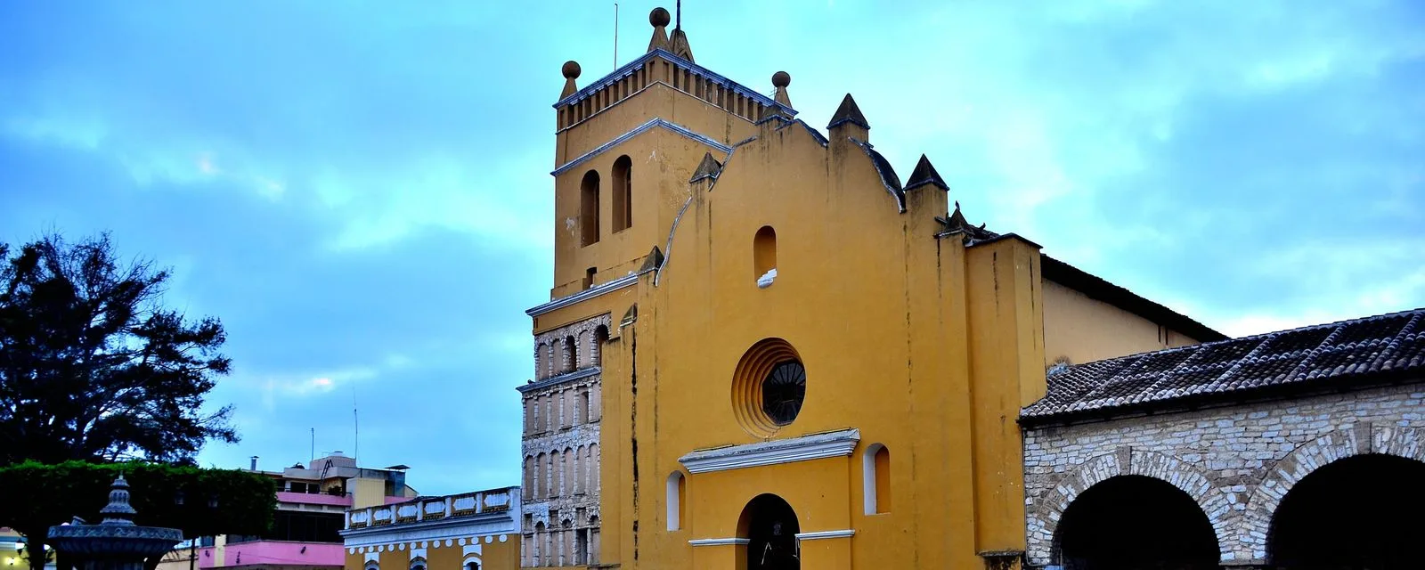 La catedral de Comitán al atardecer: su fachada amarilla de remates escalonados y su torre de cantera contra un cielo azul con nubes