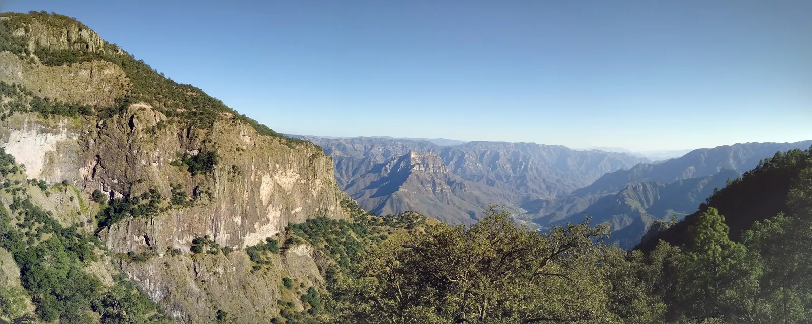 Panorámica de las Barrancas del Cobre: una pared de roca en primer plano y detrás la sucesión de cañones y sierras perdiéndose en la bruma