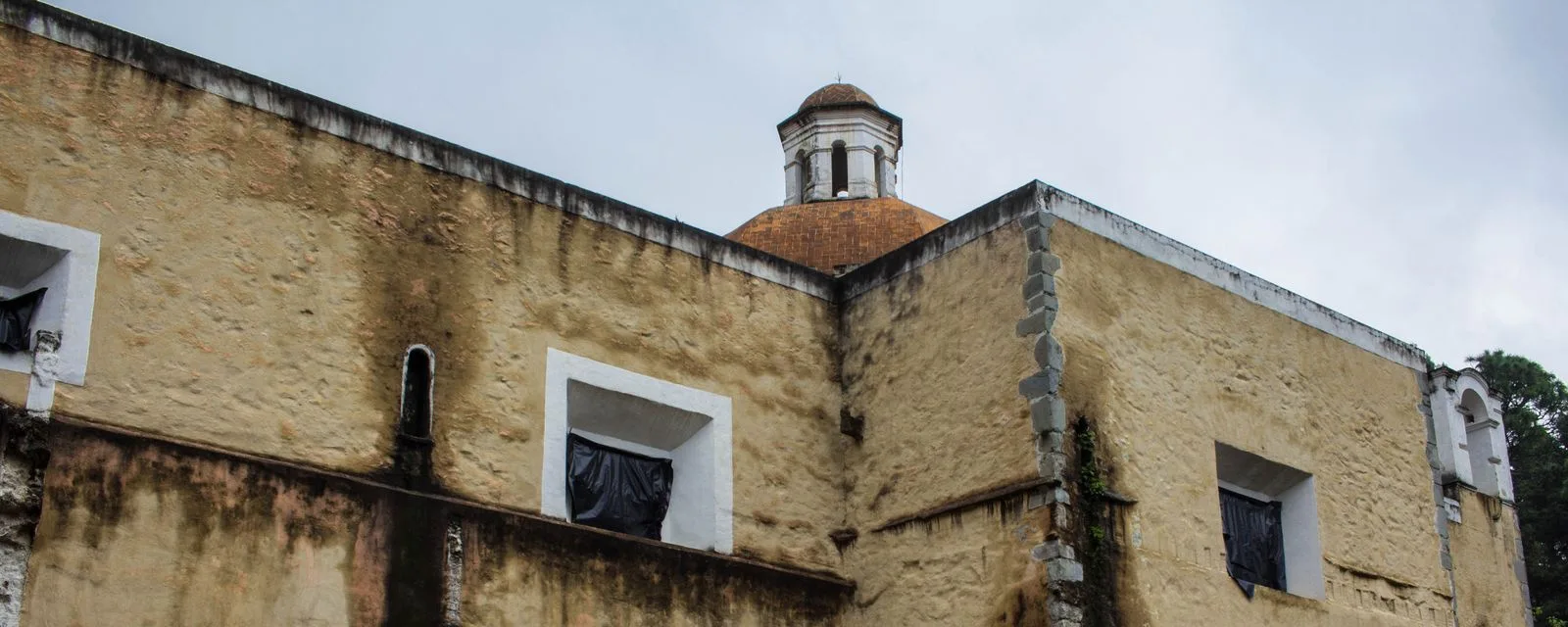 El ex convento del Desierto de los Leones visto desde fuera: muros de piedra manchados por la humedad y la cúpula de teja de la iglesia asomando detrás
