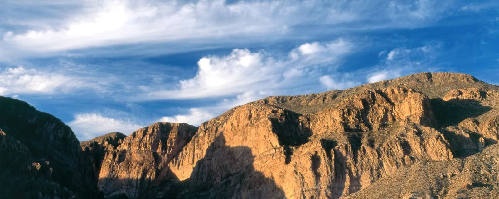 Los farallones de roca estratificada de la sierra de Múzquiz, iluminados por el sol de la tarde bajo un cielo de nubes