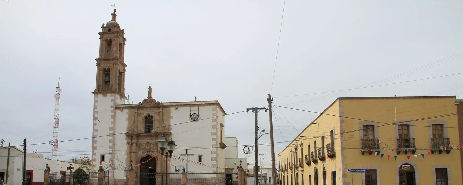 La plaza de Mapimí con la torre de la parroquia a la izquierda y la hilera de portales amarillos del costado, cruzada por papel picado