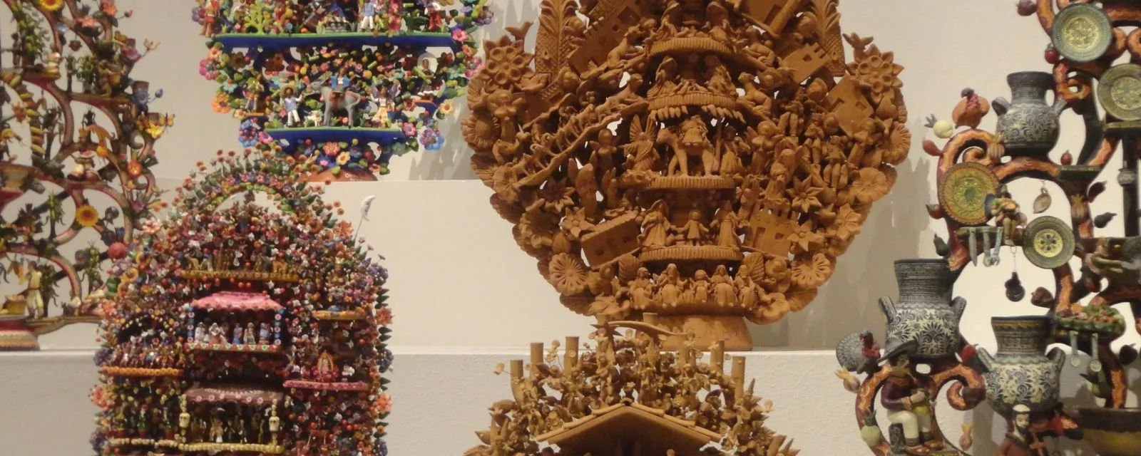 Varios árboles de la vida de barro de Metepec expuestos juntos: uno grande sin pintar, con decenas de figuras modeladas, y otros policromados alrededor