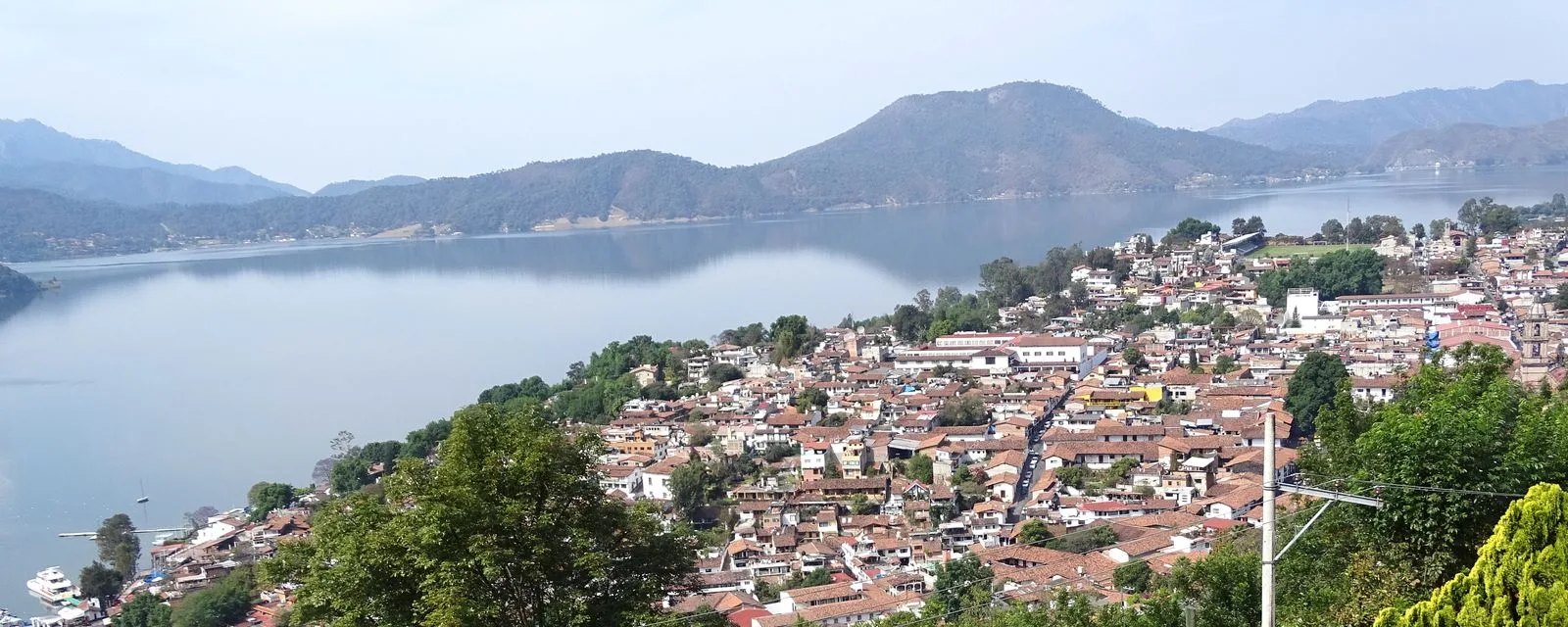 Valle de Bravo desde la altura: los techos de teja del pueblo bajando hacia el lago, con los cerros boscosos rodeando el vaso de agua