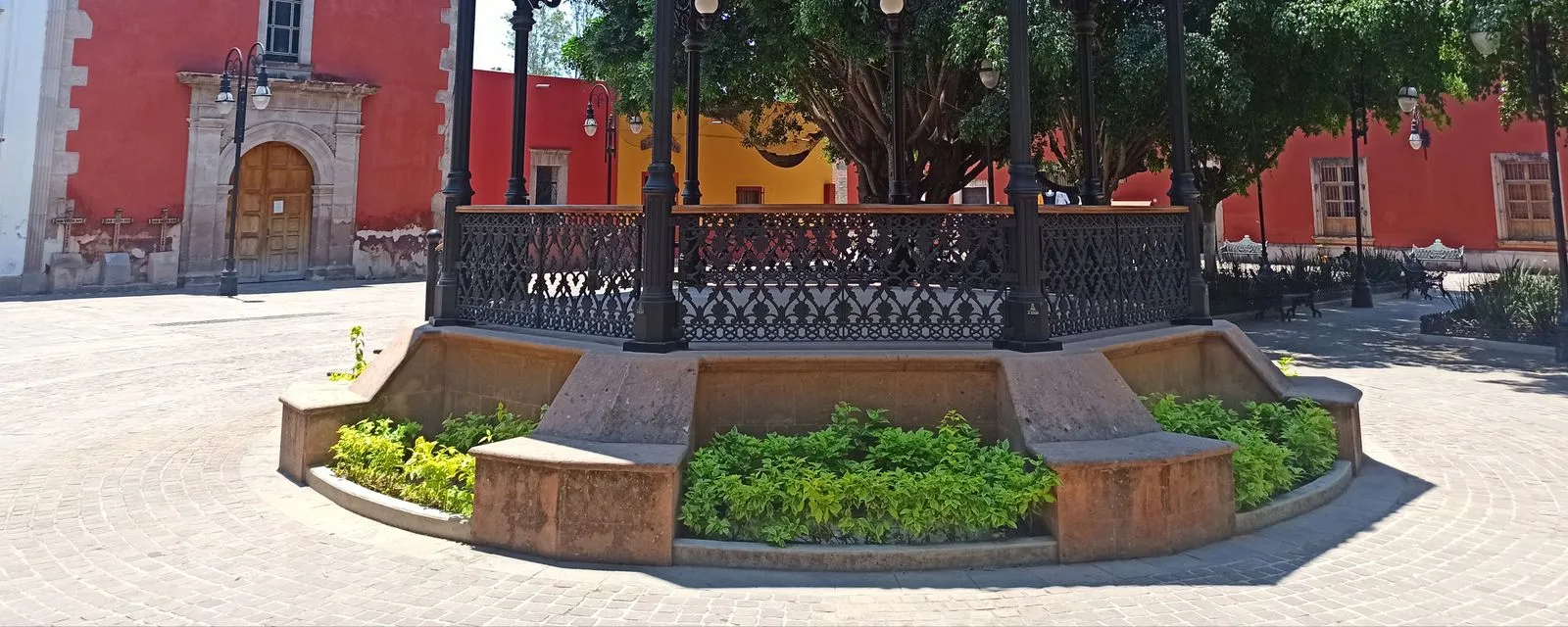 El kiosco de hierro forjado de la plaza de Jalpa de Cánovas, con las fachadas rojas y la portada de cantera del templo al fondo