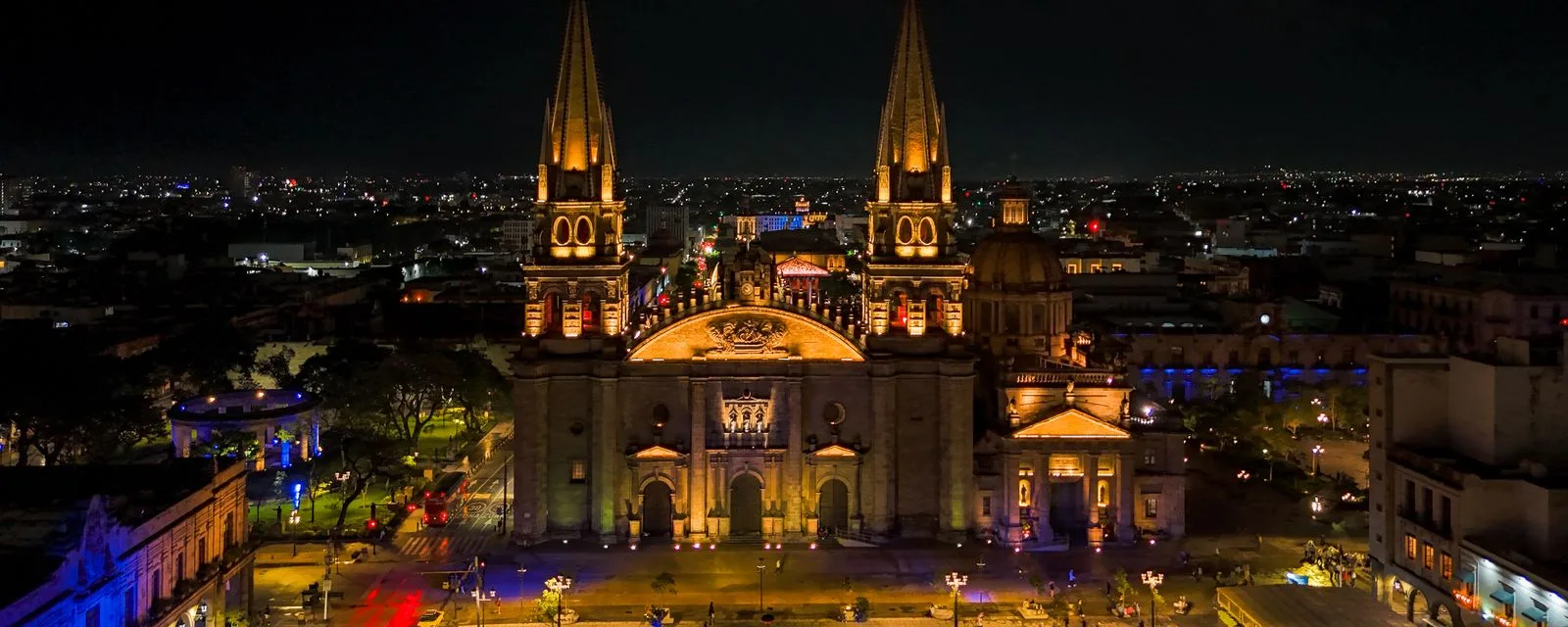 La Catedral de Guadalajara iluminada de noche vista desde el aire, con sus dos torres puntiagudas sobre el centro histórico encendido