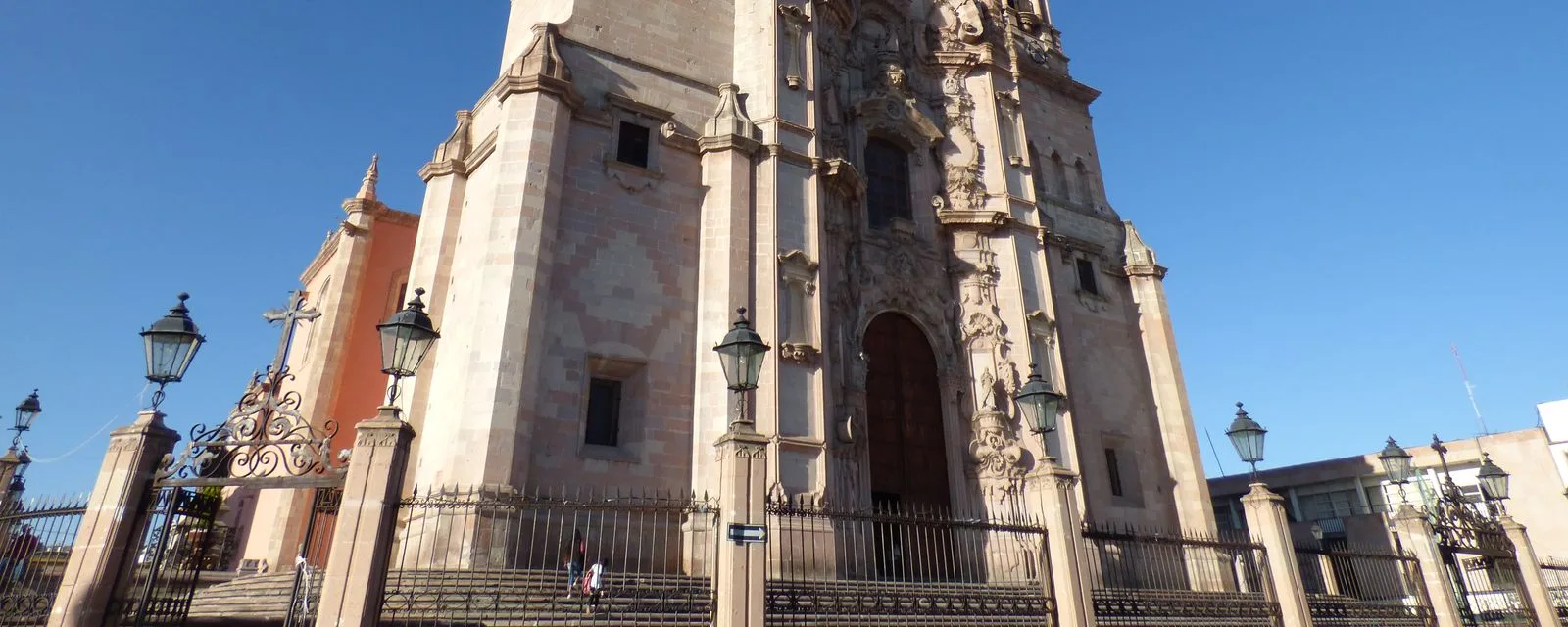 La parroquia de Nuestra Señora de la Asunción de Lagos de Moreno vista desde el atrio: su portada churrigueresca de cantera rosa y la reja de hierro al frente