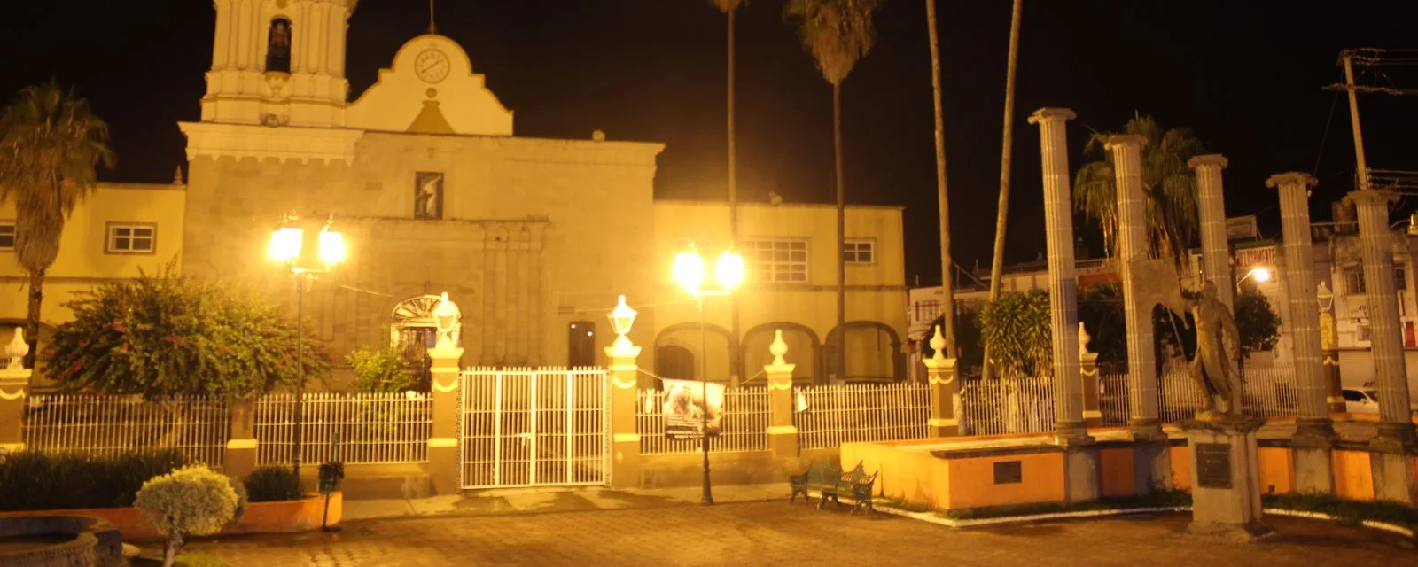 La basílica de Talpa de Allende iluminada de noche, vista desde la plaza con sus faroles y las palmeras del jardín