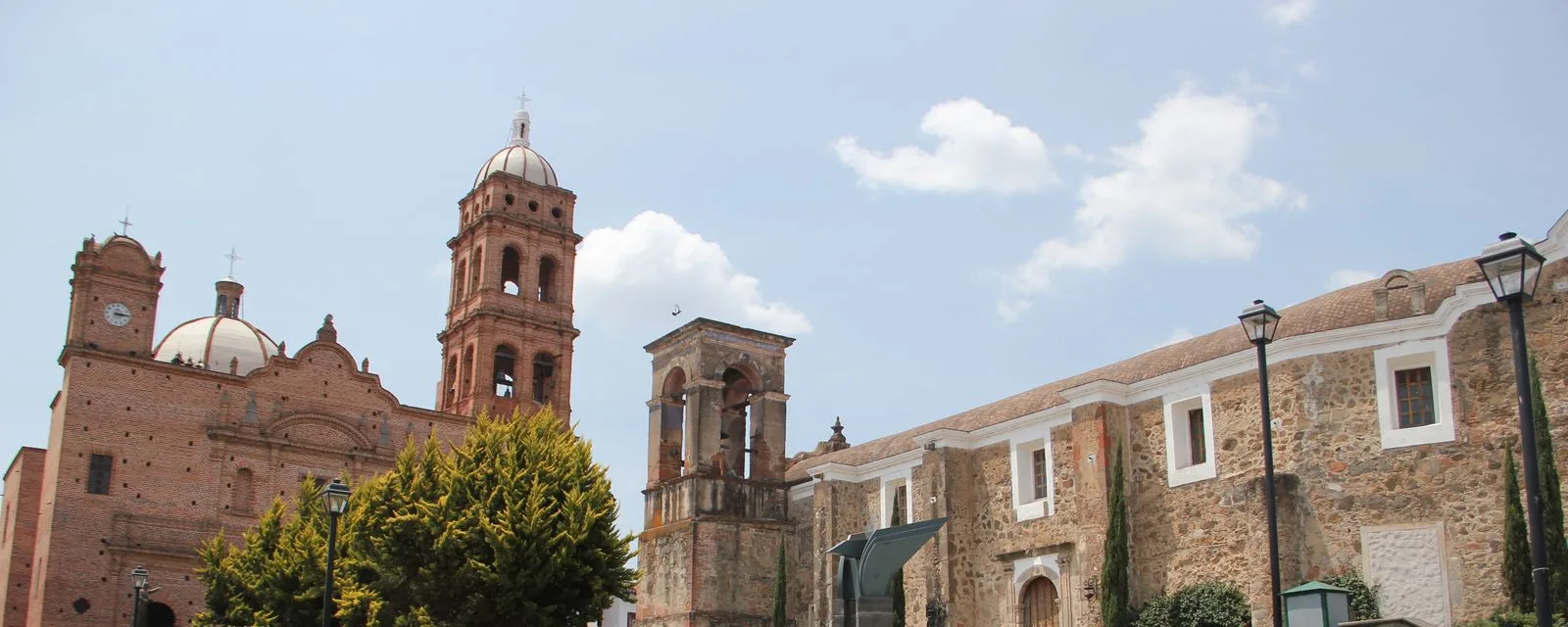 El conjunto religioso de Tapalpa: el templo de la Inmaculada Concepción de ladrillo rojo con su torre y su cúpula, junto a los muros de piedra de la antigua parroquia