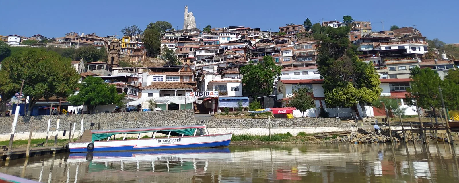 La isla de Janitzio desde el agua: las casas de teja trepando el cerro y la estatua de Morelos coronando la cima