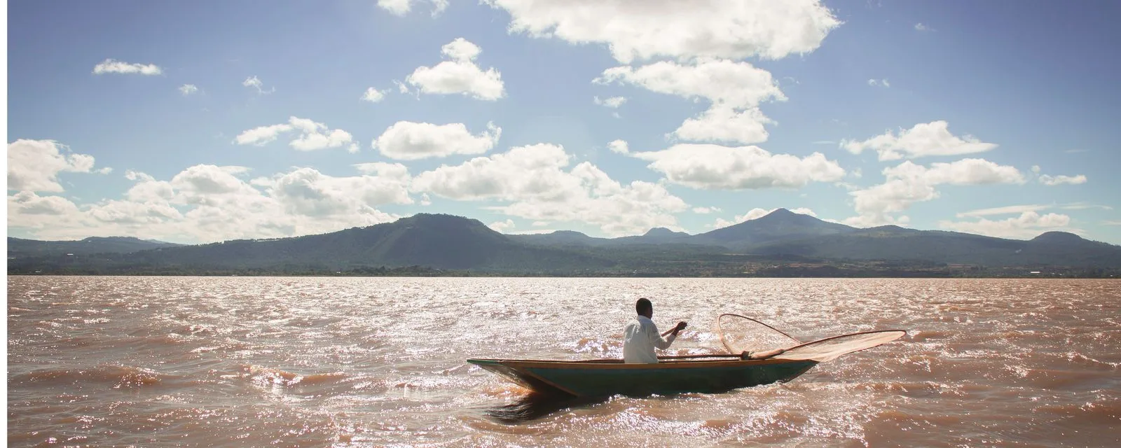 Un pescador rema solo en el lago de Pátzcuaro con su red de mariposa recogida en la proa, con la sierra michoacana al fondo