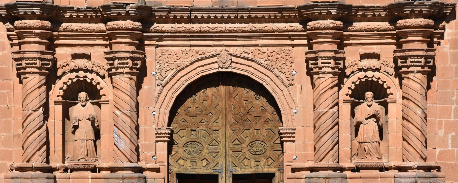 Detalle de la portada del Santuario del Carmen en Tlalpujahua: cantera rosa labrada con columnas salomónicas y dos esculturas en sus nichos, sobre el portón de madera
