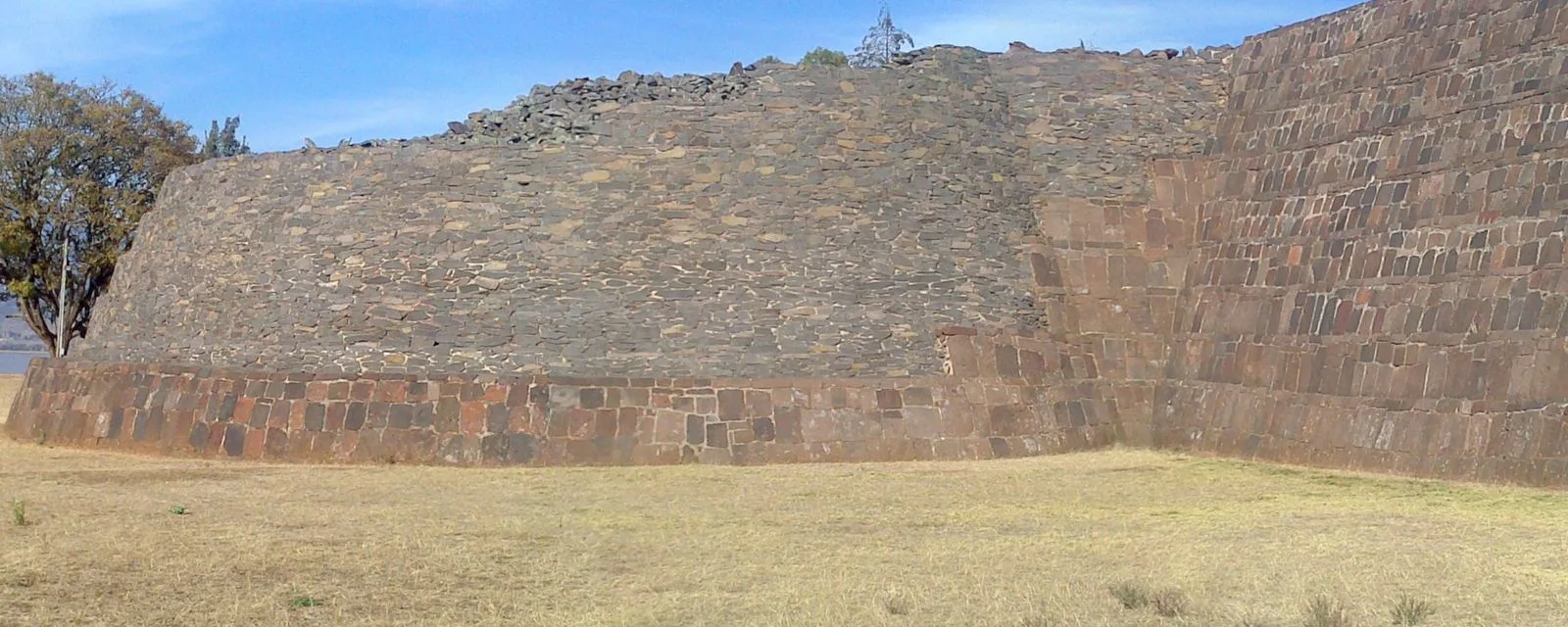 Una yácata de Tzintzuntzan: el basamento purépecha de planta redondeada, con su muro de lajas de piedra sobre un zócalo de bloques rojizos