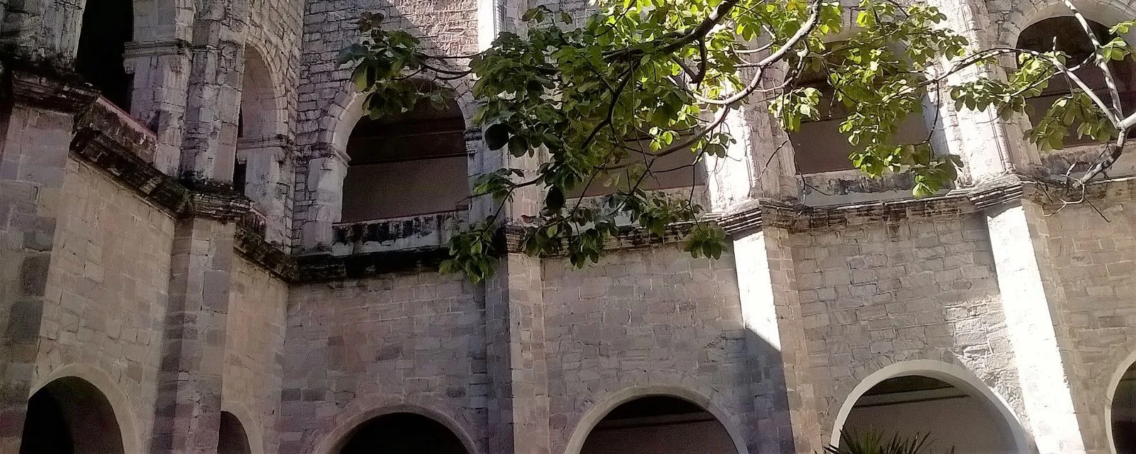 El claustro de dos niveles del ex convento de Santo Domingo en Oaxtepec: arcadas de piedra con las ramas de un árbol asomando por los vanos