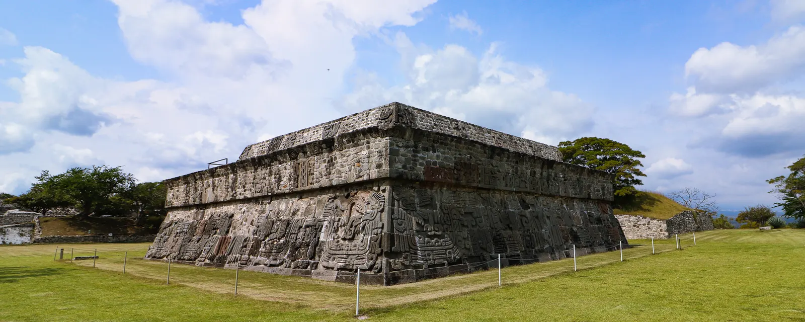La Pirámide de las Serpientes Emplumadas de Xochicalco vista de esquina, con sus relieves labrados sobre el talud y el pasto de la explanada alrededor