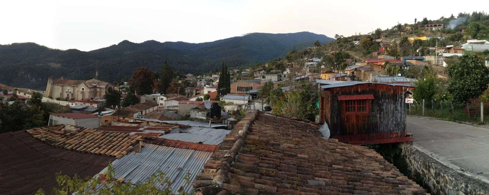 Capulálpam de Méndez visto sobre los techos de teja y lámina del pueblo, con el templo a la izquierda y la sierra de Juárez cerrando el fondo