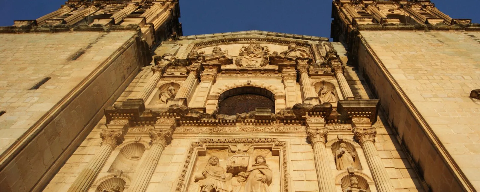 La fachada del Templo de Santo Domingo de Guzmán en Oaxaca vista desde el atrio: dos torres de cantera y el relieve central con esculturas en sus nichos
