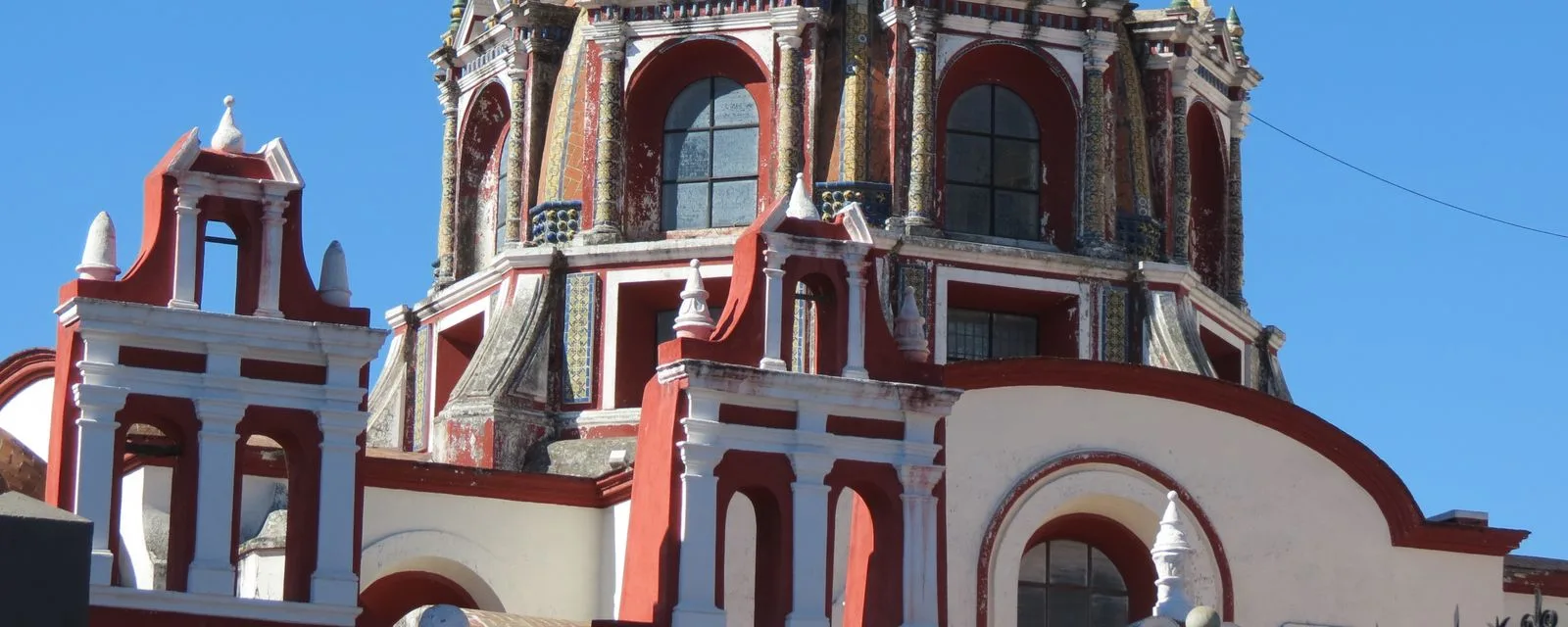 La cúpula exterior de la Capilla del Rosario vista desde la calle: tambor de ventanas y volutas pintadas de rojo y blanco con azulejo entre los nervios