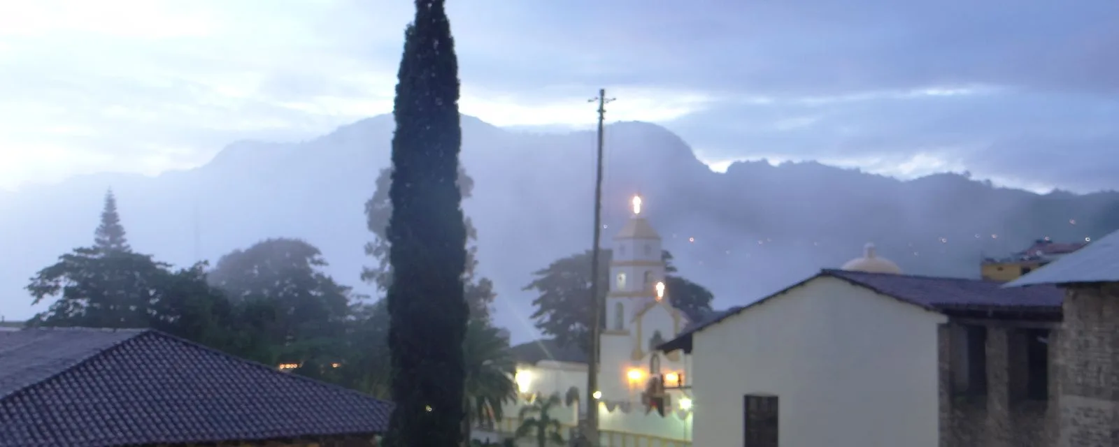 Pahuatlán entre la neblina al anochecer: la torre iluminada de la iglesia de Santiago Apóstol sobre los tejados, con la sierra difuminada detrás