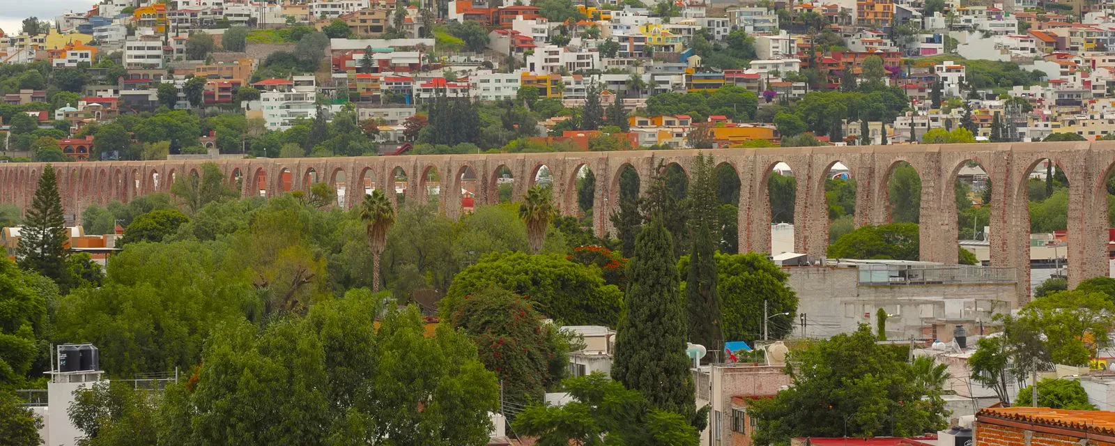 La arquería del acueducto de Querétaro cruzando la imagen de lado a lado, con las casas de colores del cerro subiendo detrás
