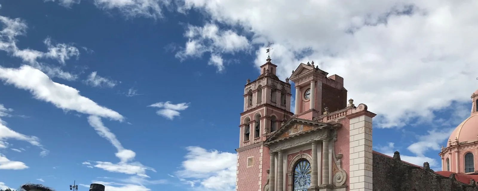 La parroquia de Santa María de la Asunción en Tequisquiapan: torre y portada de cantera rosa recortadas contra un cielo azul con nubes