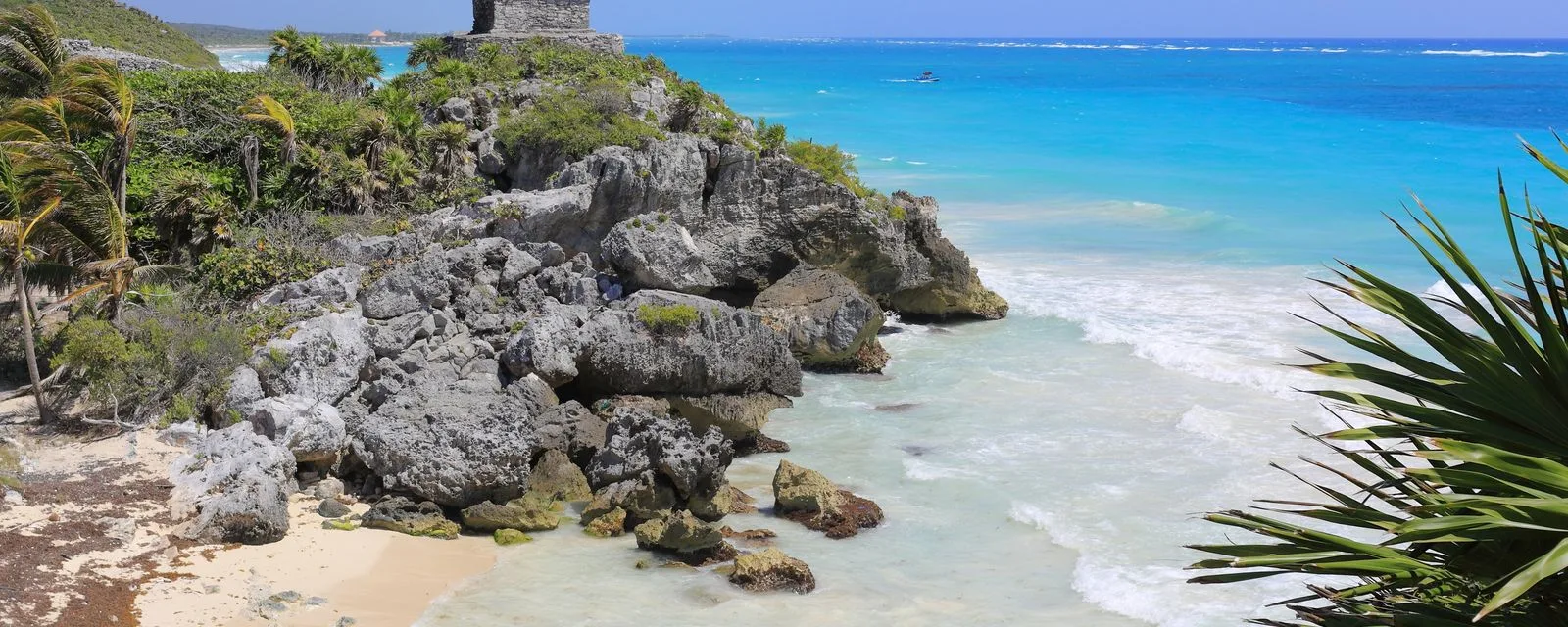 La costa de Tulum: el acantilado de roca sobre la playa, el mar turquesa rompiendo abajo y un templo maya asomando entre las palmas