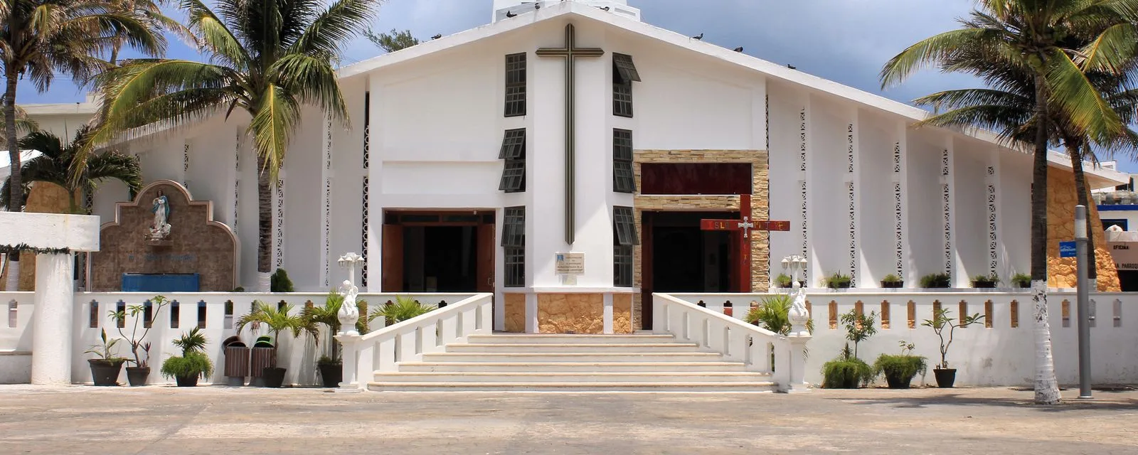 La iglesia de la Inmaculada Concepción de Isla Mujeres: fachada blanca de dos aguas con una cruz de madera, flanqueada por palmeras