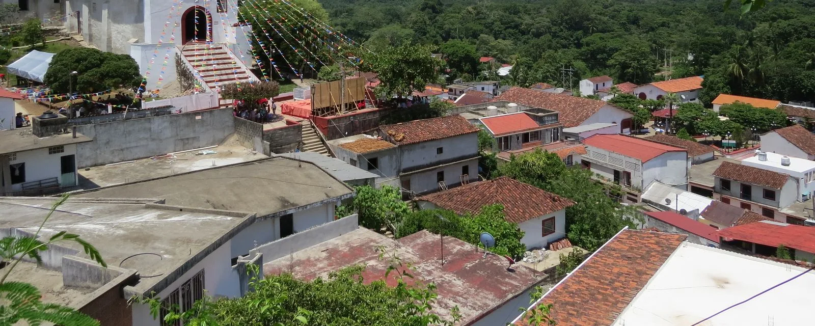 Tapijulapa desde lo alto: los techos de teja del pueblo escalonados por la ladera y la escalinata blanca de la iglesia adornada con papel picado