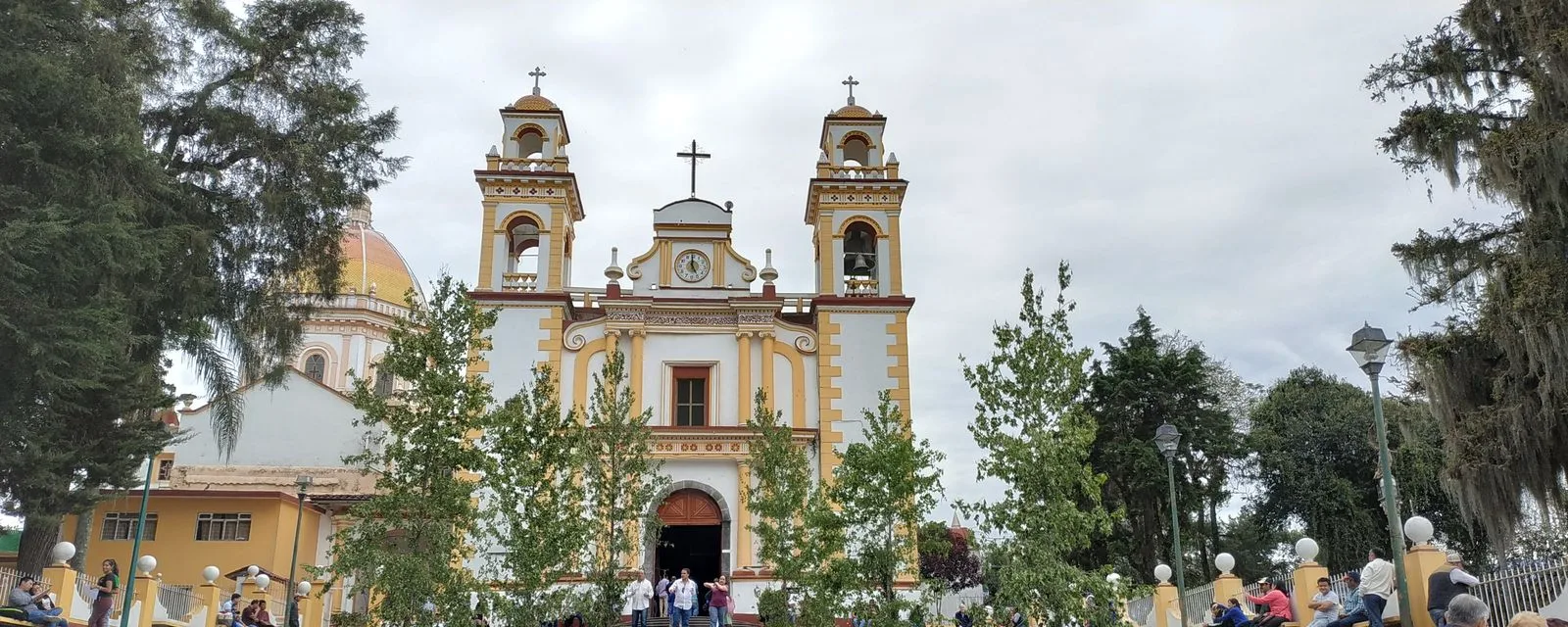 La parroquia de Santa María Magdalena de Xico vista de frente: fachada blanca con molduras amarillas, dos campanarios y la cúpula asomando a un costado