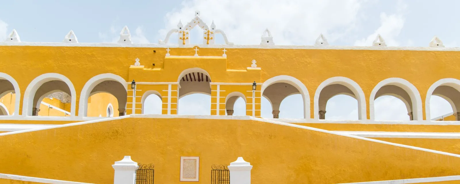 El convento de San Antonio de Padua en Izamal: su muro y su arquería pintados de amarillo con las molduras en blanco, bajo el cielo despejado